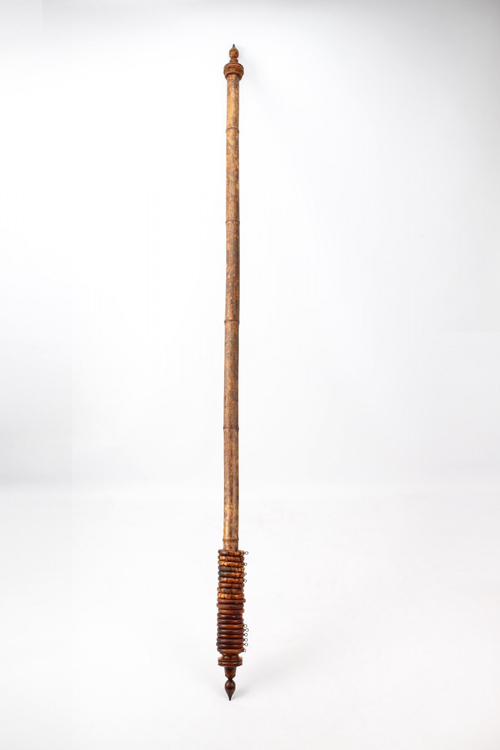A long natural bamboo curtain pole featuring turned wooden finials at both ends and a set of matching wooden curtain rings stacked near one end.
