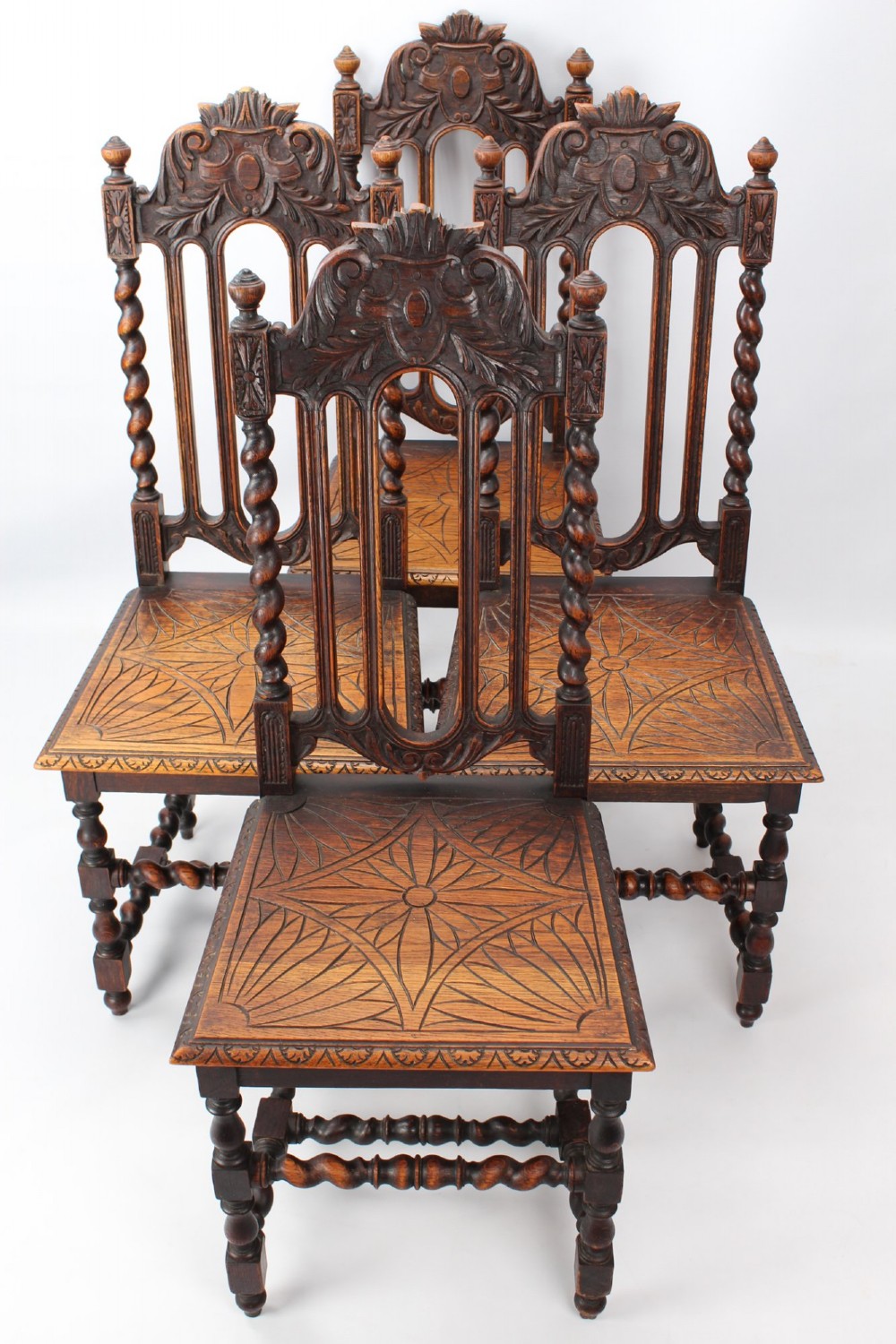 A set of four Victorian Gothic Revival dark oak chairs featuring carved floral crestings, barley twist supports, and carved geometric patterned wooden seats.