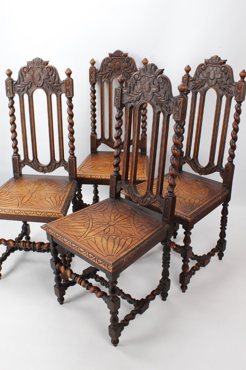 A set of four Victorian Gothic Revival dark oak chairs featuring carved floral crestings, barley twist supports, and carved geometric patterned wooden seats. View II