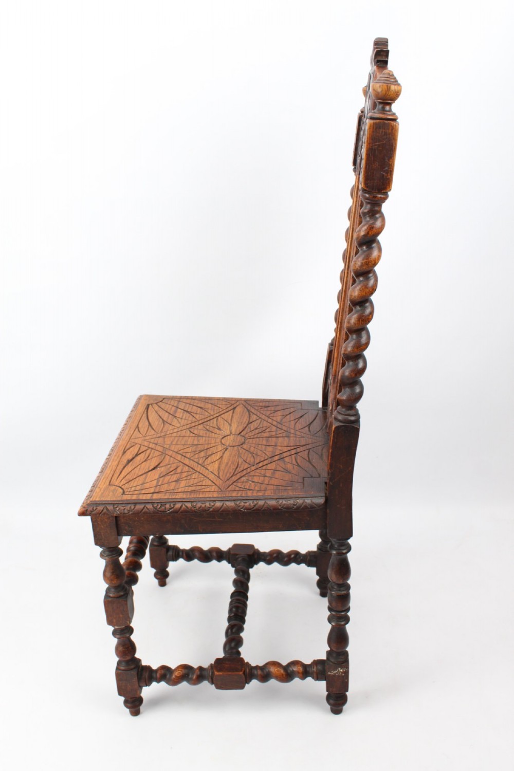 A set of four Victorian Gothic Revival dark oak chairs featuring carved floral crestings, barley twist supports, and carved geometric patterned wooden seats. View V