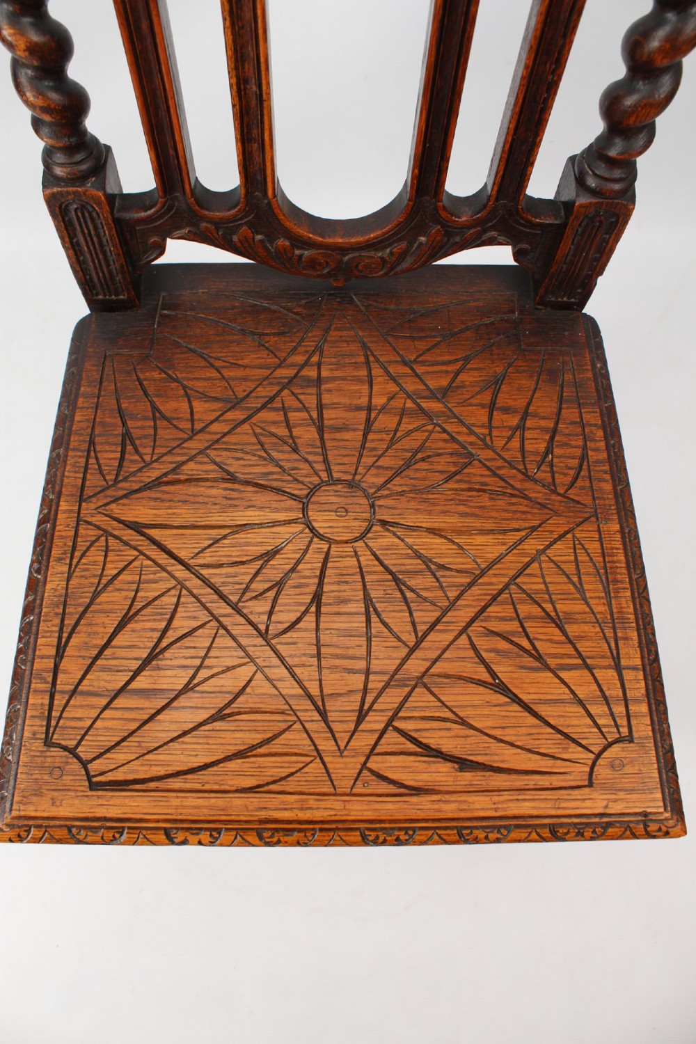 A set of four Victorian Gothic Revival dark oak chairs featuring carved floral crestings, barley twist supports, and carved geometric patterned wooden seats. View IX