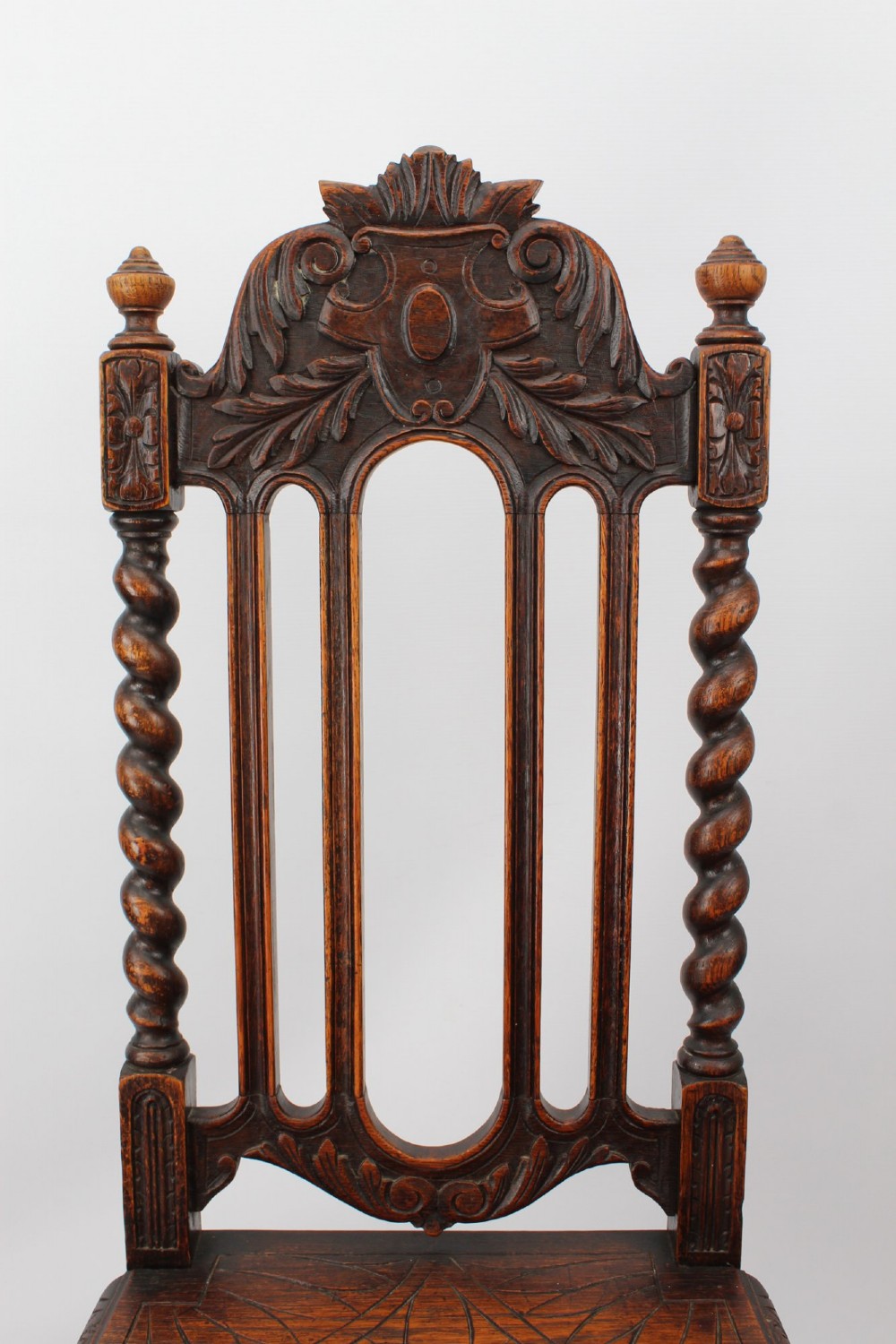 A set of four Victorian Gothic Revival dark oak chairs featuring carved floral crestings, barley twist supports, and carved geometric patterned wooden seats. View X