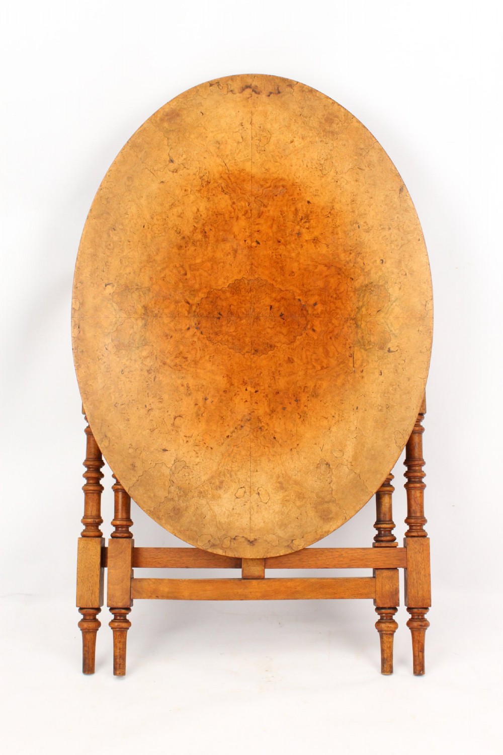 A Victorian burr walnut oval table shown with its top tilted vertically on a wooden frame with turned legs.