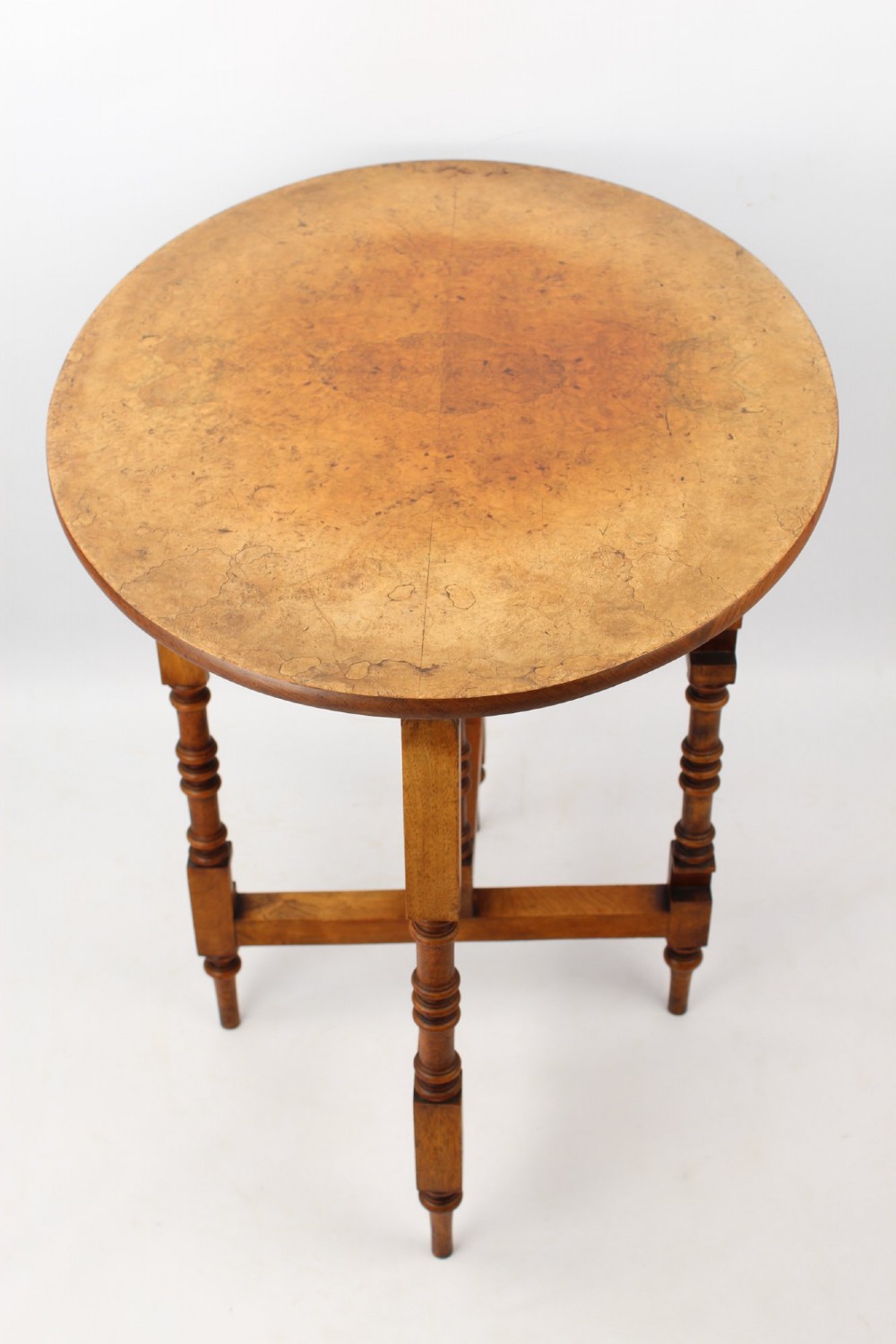 A Victorian burr walnut oval table shown with its top tilted vertically on a wooden frame with turned legs. View III