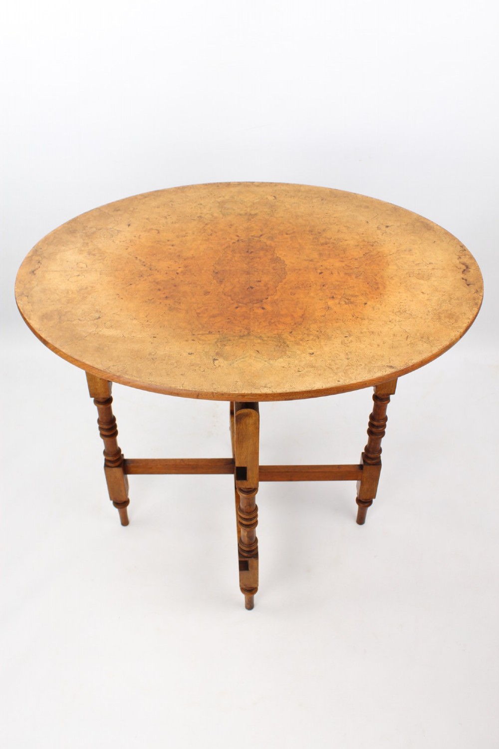 A Victorian burr walnut oval table shown with its top tilted vertically on a wooden frame with turned legs. View IV