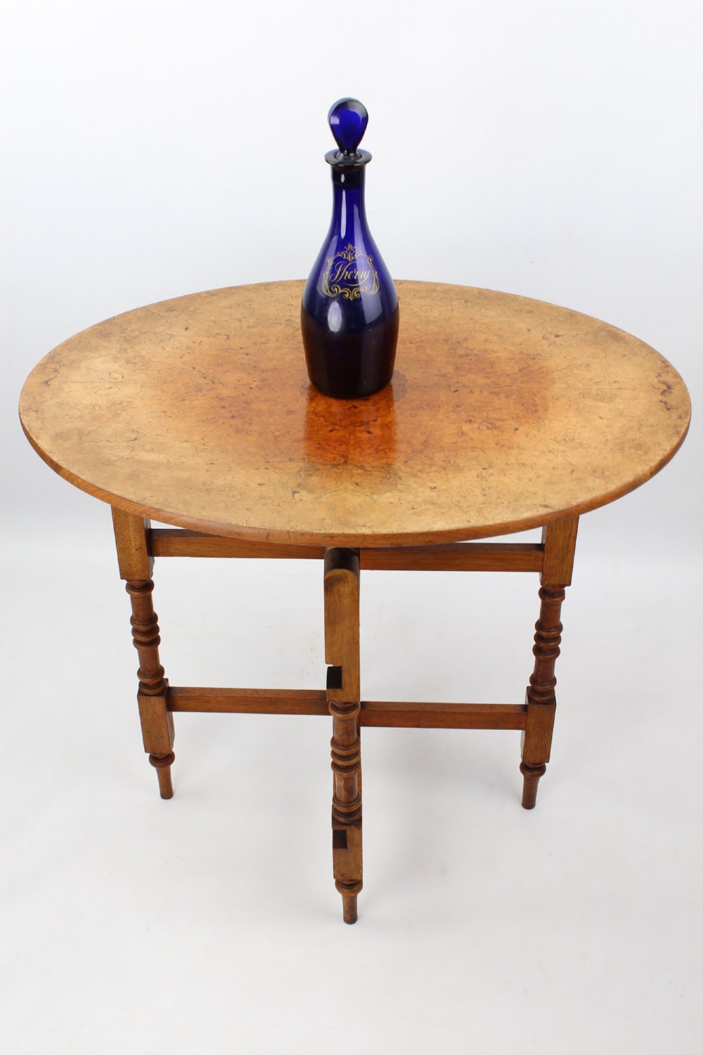 A Victorian burr walnut oval table shown with its top tilted vertically on a wooden frame with turned legs. View XIII