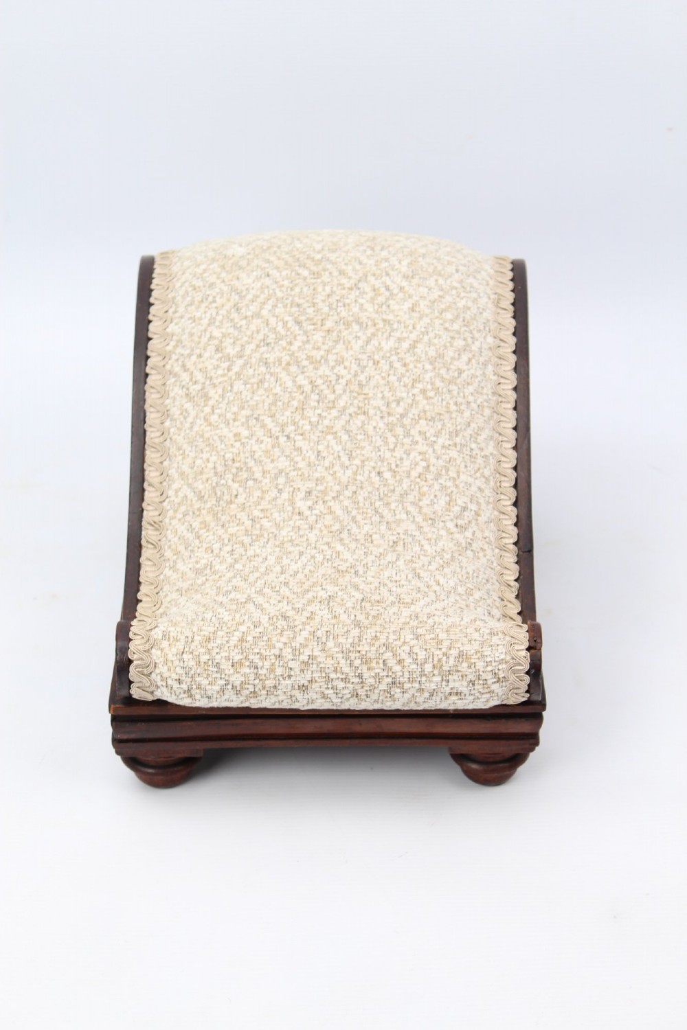An inclined Regency rosewood footstool featuring carved side scrolls, turned bun feet, and cream textured upholstery finished with gimp braid. View II