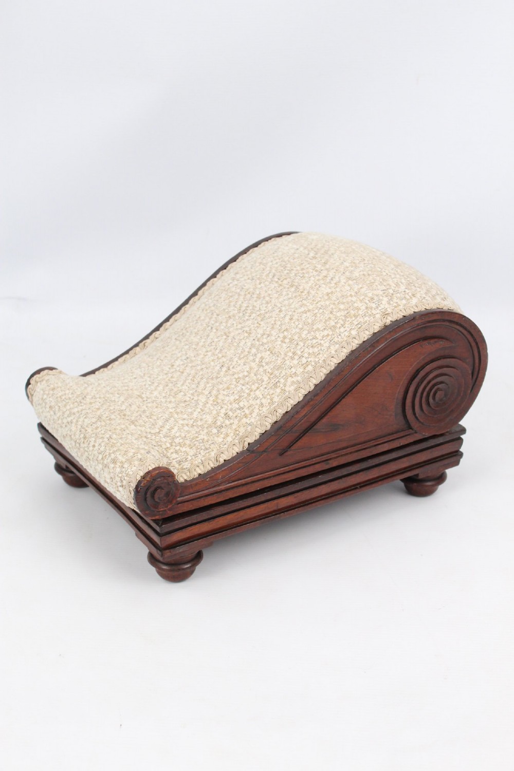 An inclined Regency rosewood footstool featuring carved side scrolls, turned bun feet, and cream textured upholstery finished with gimp braid. View III