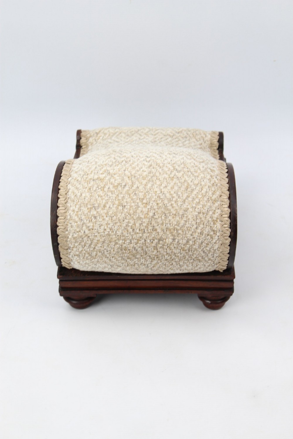 An inclined Regency rosewood footstool featuring carved side scrolls, turned bun feet, and cream textured upholstery finished with gimp braid. View VI