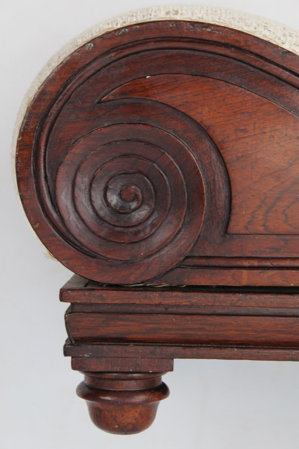 An inclined Regency rosewood footstool featuring carved side scrolls, turned bun feet, and cream textured upholstery finished with gimp braid. View VIII