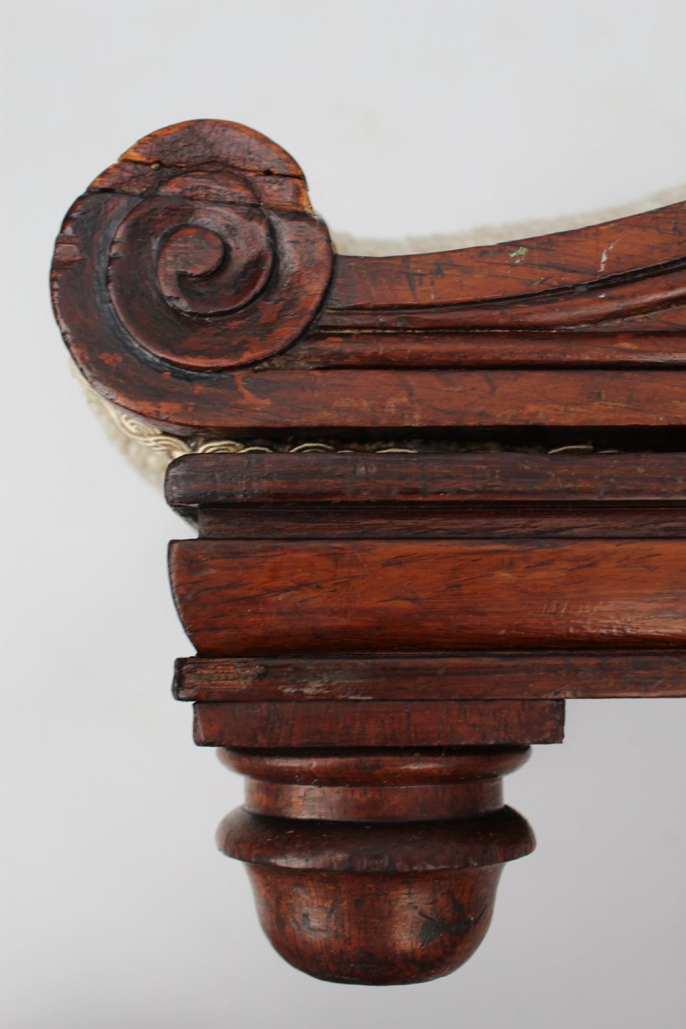 An inclined Regency rosewood footstool featuring carved side scrolls, turned bun feet, and cream textured upholstery finished with gimp braid. View XI