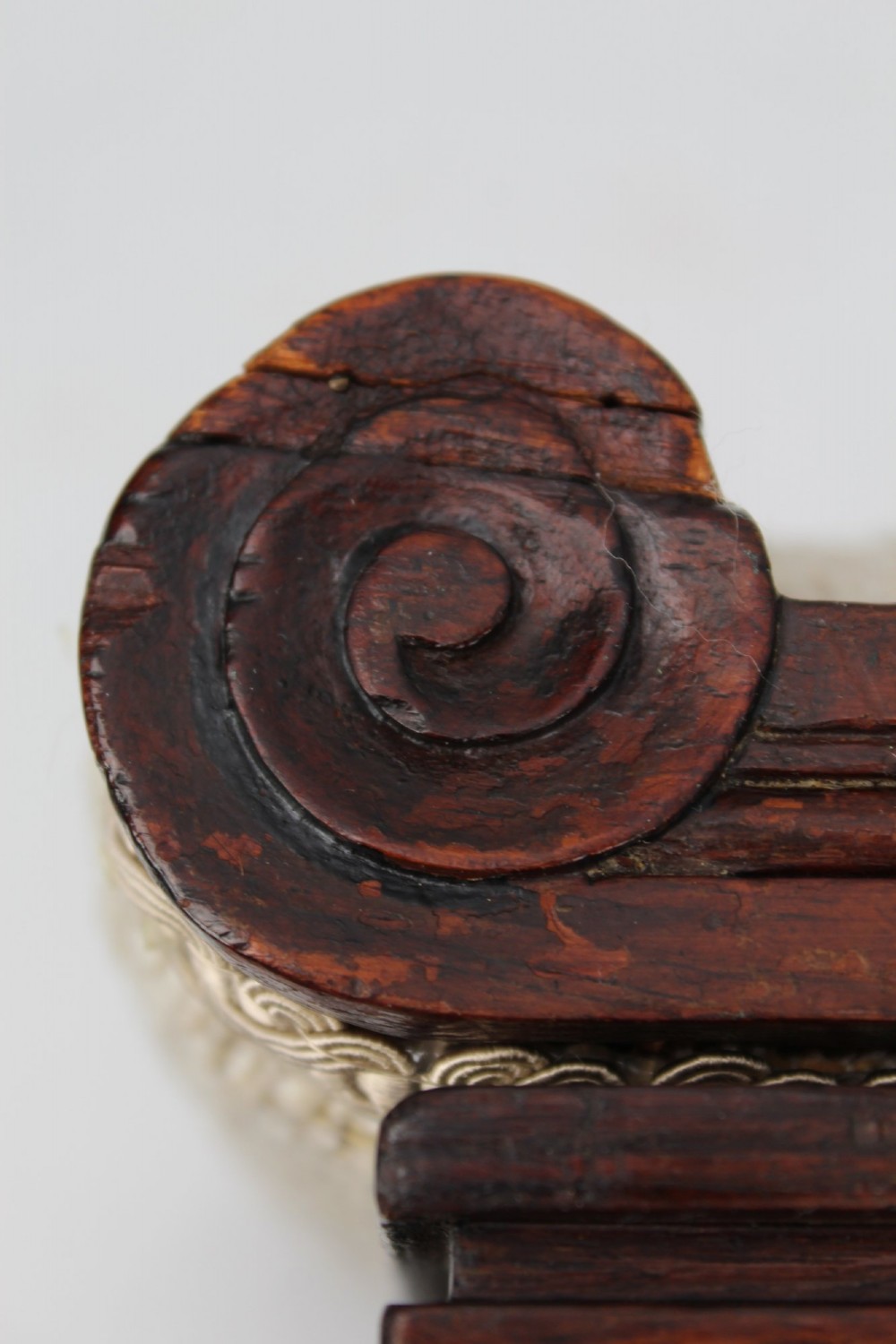 An inclined Regency rosewood footstool featuring carved side scrolls, turned bun feet, and cream textured upholstery finished with gimp braid. View XII