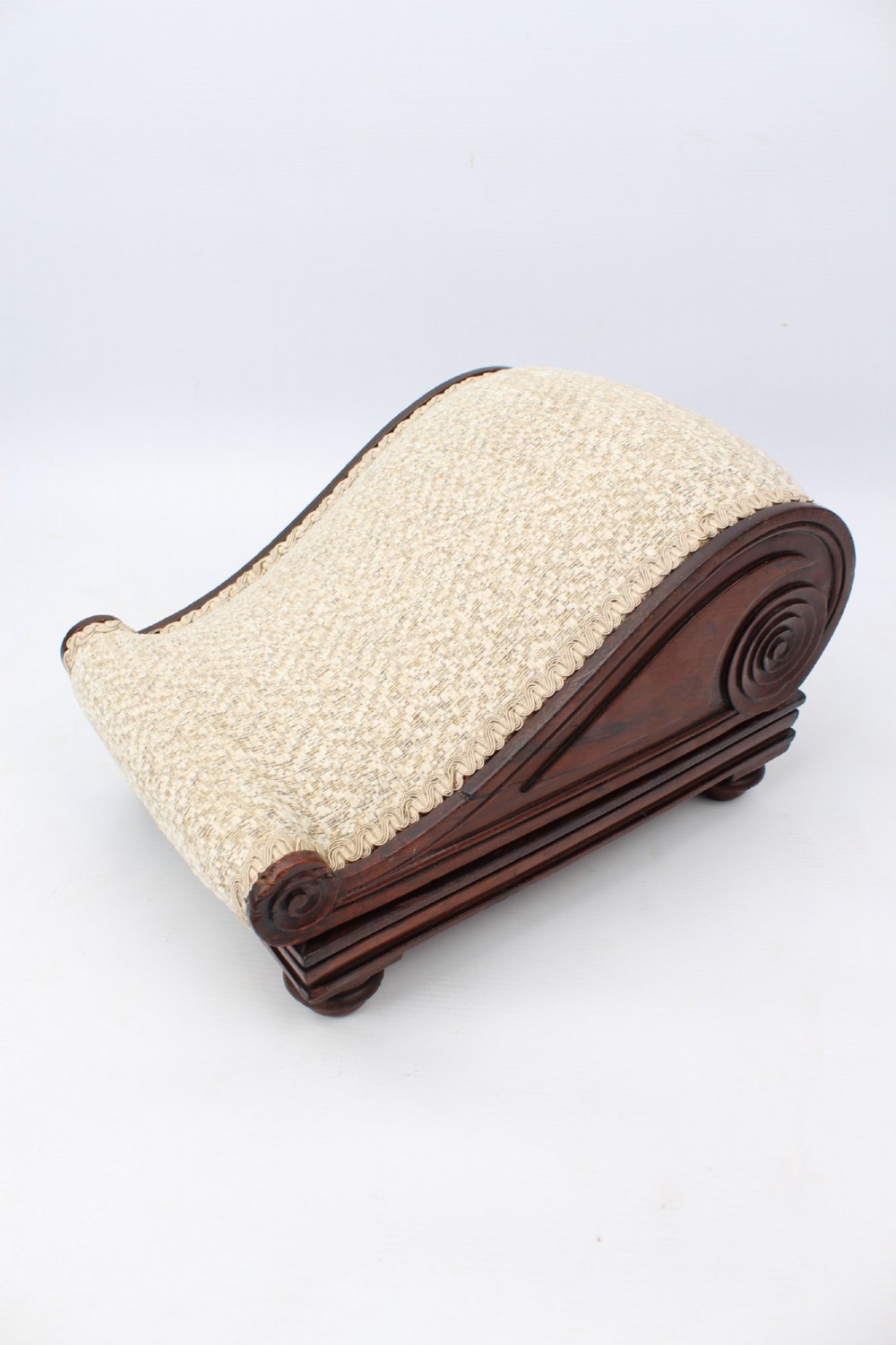 An inclined Regency rosewood footstool featuring carved side scrolls, turned bun feet, and cream textured upholstery finished with gimp braid. View XIII