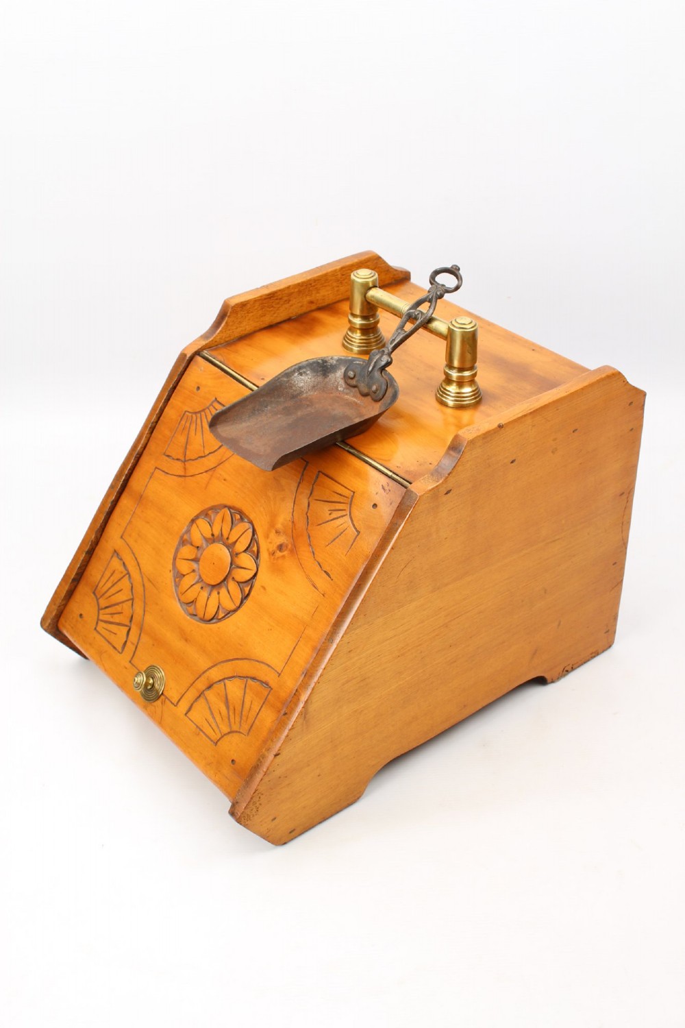 A slant-front Victorian wooden coal scuttle featuring carved floral motifs, a brass top handle, and a metal shovel stowed at the back. View V