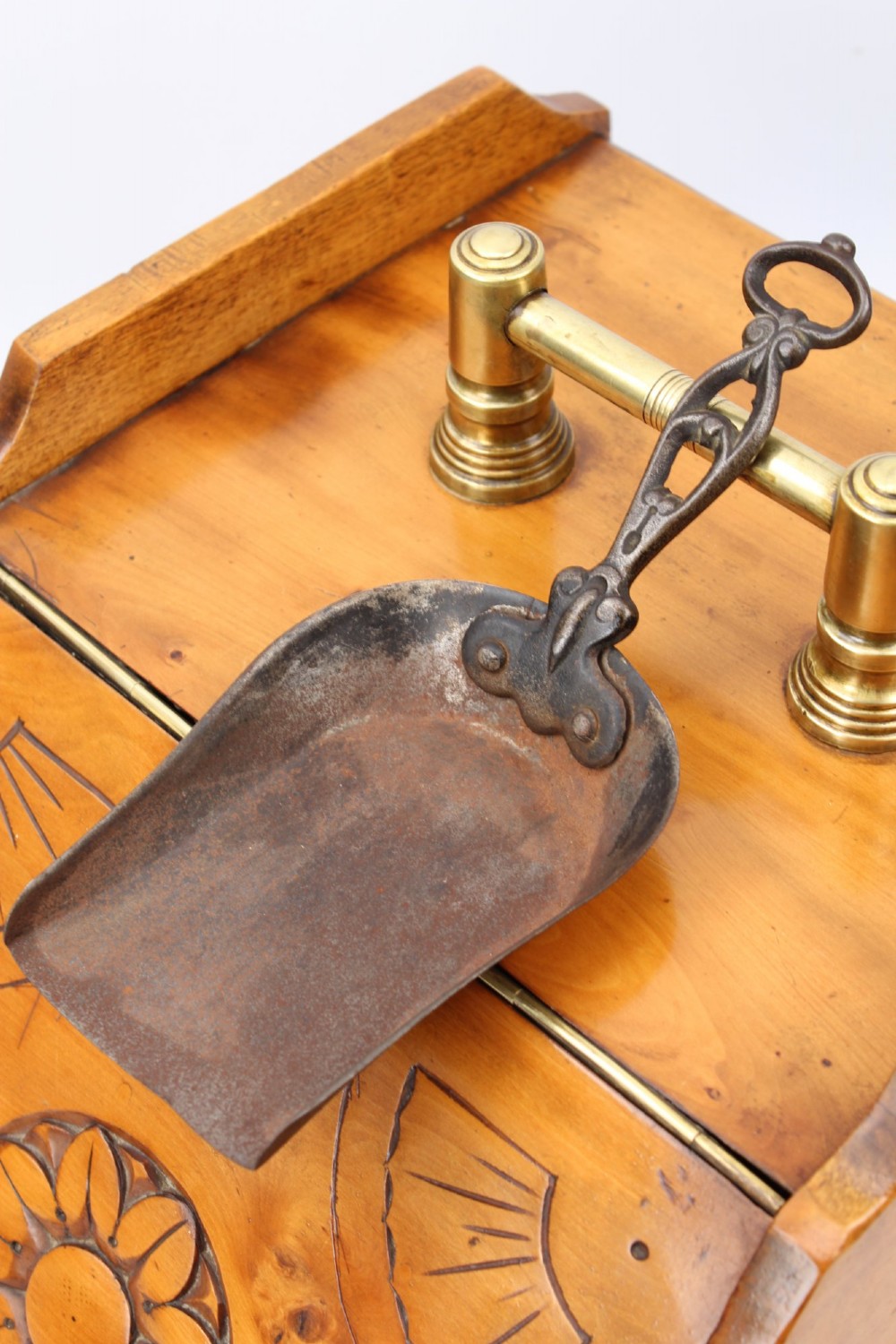A slant-front Victorian wooden coal scuttle featuring carved floral motifs, a brass top handle, and a metal shovel stowed at the back. View VI