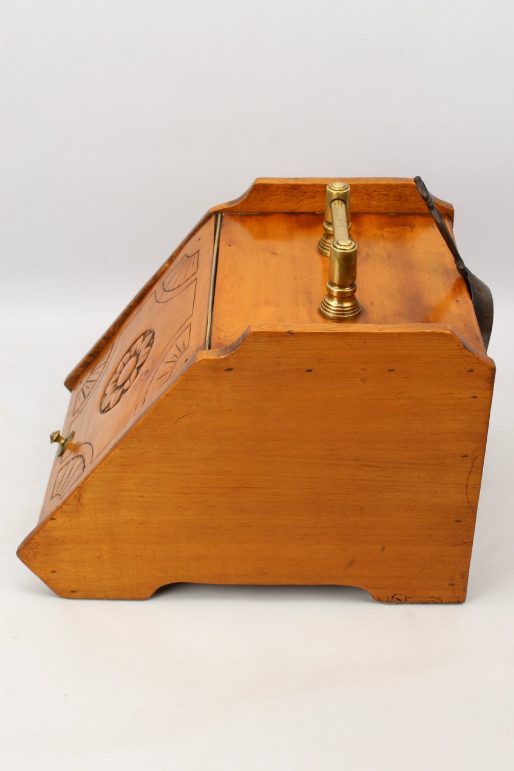 A slant-front Victorian wooden coal scuttle featuring carved floral motifs, a brass top handle, and a metal shovel stowed at the back. View VIII