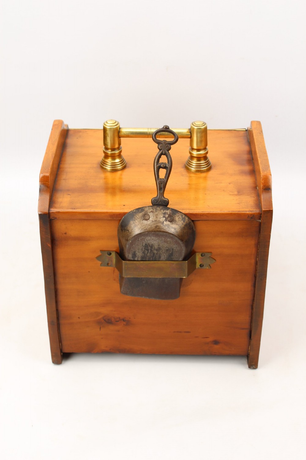A slant-front Victorian wooden coal scuttle featuring carved floral motifs, a brass top handle, and a metal shovel stowed at the back. View IX