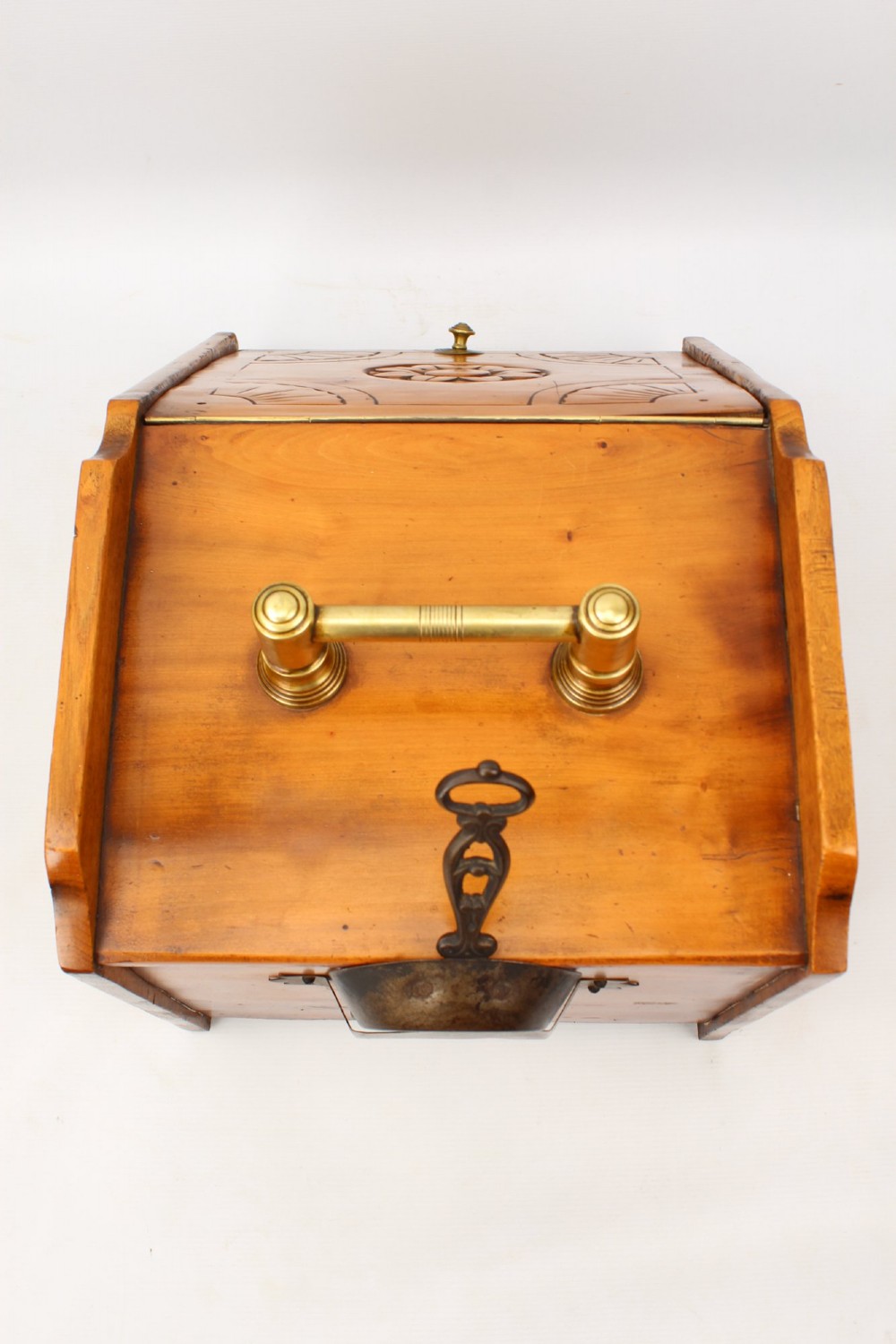 A slant-front Victorian wooden coal scuttle featuring carved floral motifs, a brass top handle, and a metal shovel stowed at the back. View X