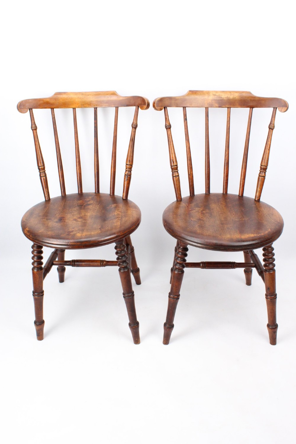 A pair of warm brown wooden kitchen chairs featuring spindle backs, turned legs, and solid timber seats.