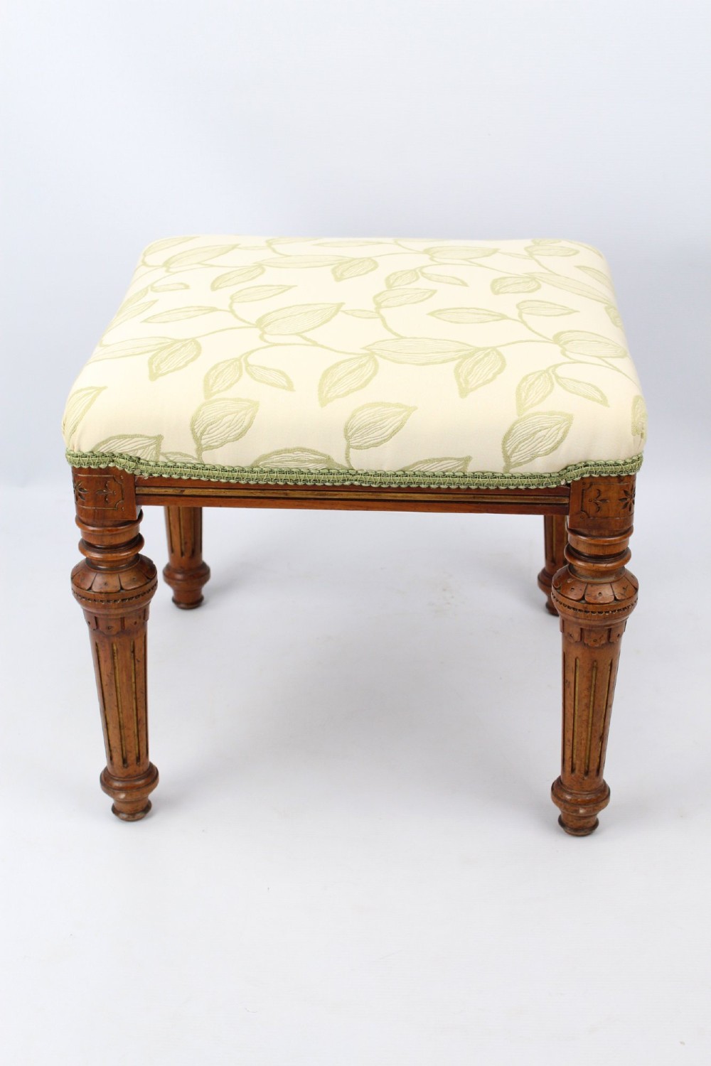 A square Victorian oak dressing stool featuring fluted turned legs with gilt accents and a cream fabric seat decorated with green leaf motifs. View III