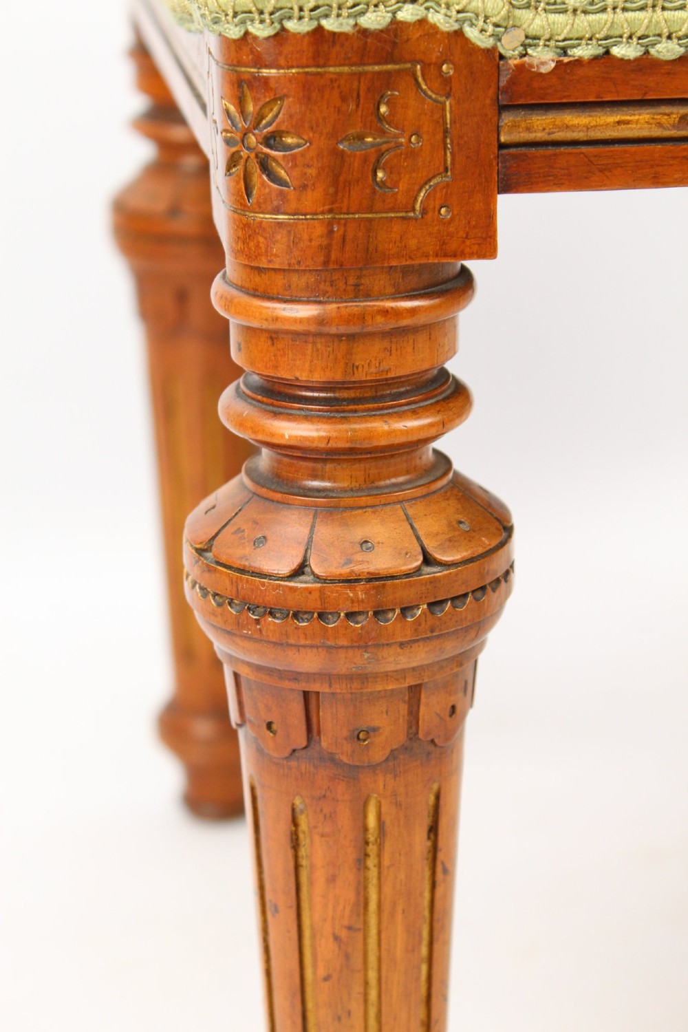 A square Victorian oak dressing stool featuring fluted turned legs with gilt accents and a cream fabric seat decorated with green leaf motifs. View IV