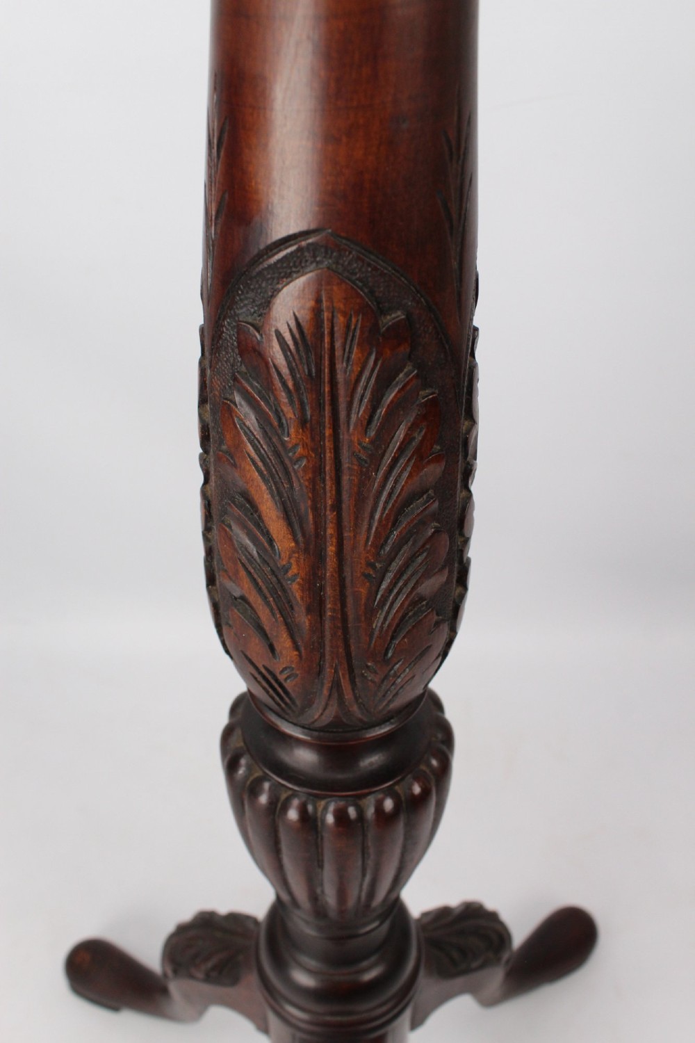 A tall Edwardian mahogany plant stand with a circular top, carved acanthus leaf column, and a tripod base. View IX