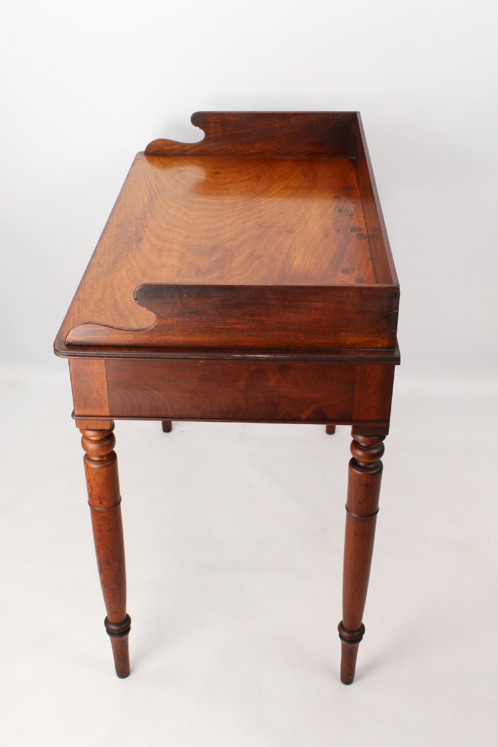 A Victorian mahogany writing table featuring a low gallery back top, two frieze drawers with decorative handles, and four turned legs. View IV