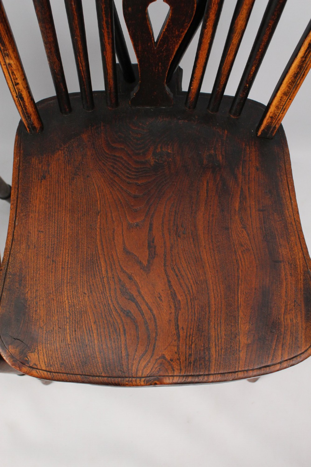 A near pair of antique dark timber Windsor kitchen chairs featuring pierced wheelback splats, contoured saddle seats, and turned legs. View III