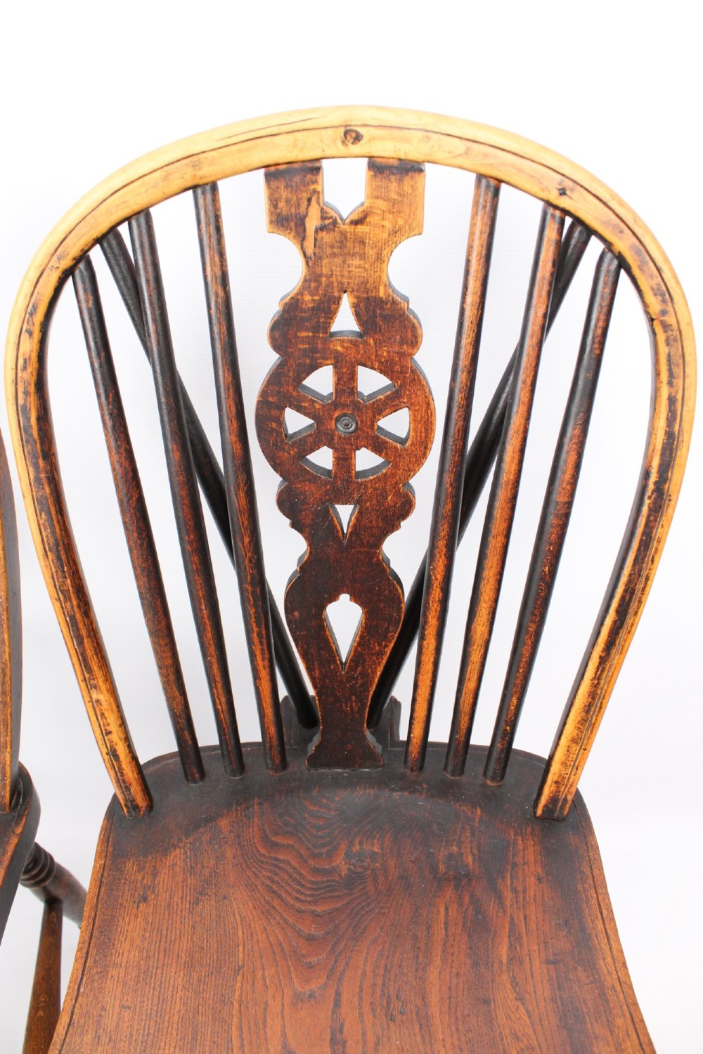 A near pair of antique dark timber Windsor kitchen chairs featuring pierced wheelback splats, contoured saddle seats, and turned legs. View V