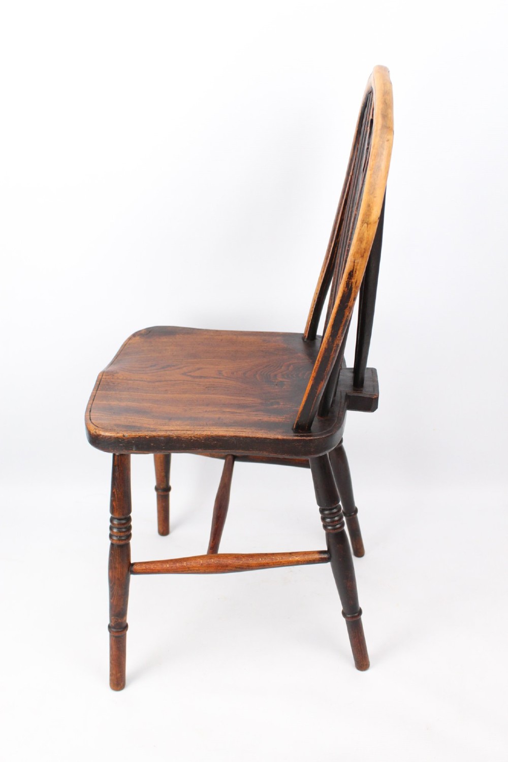 A near pair of antique dark timber Windsor kitchen chairs featuring pierced wheelback splats, contoured saddle seats, and turned legs. View X