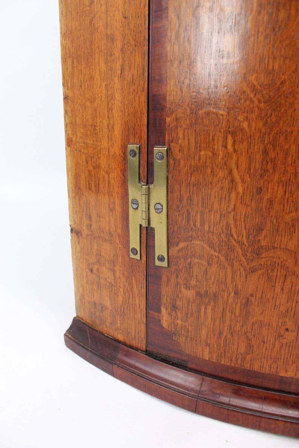 An 18th-century Georgian oak corner cupboard featuring a curved bow front, brass H-hinges, keyhole escutcheon plates, and mahogany crossbanding. View XI