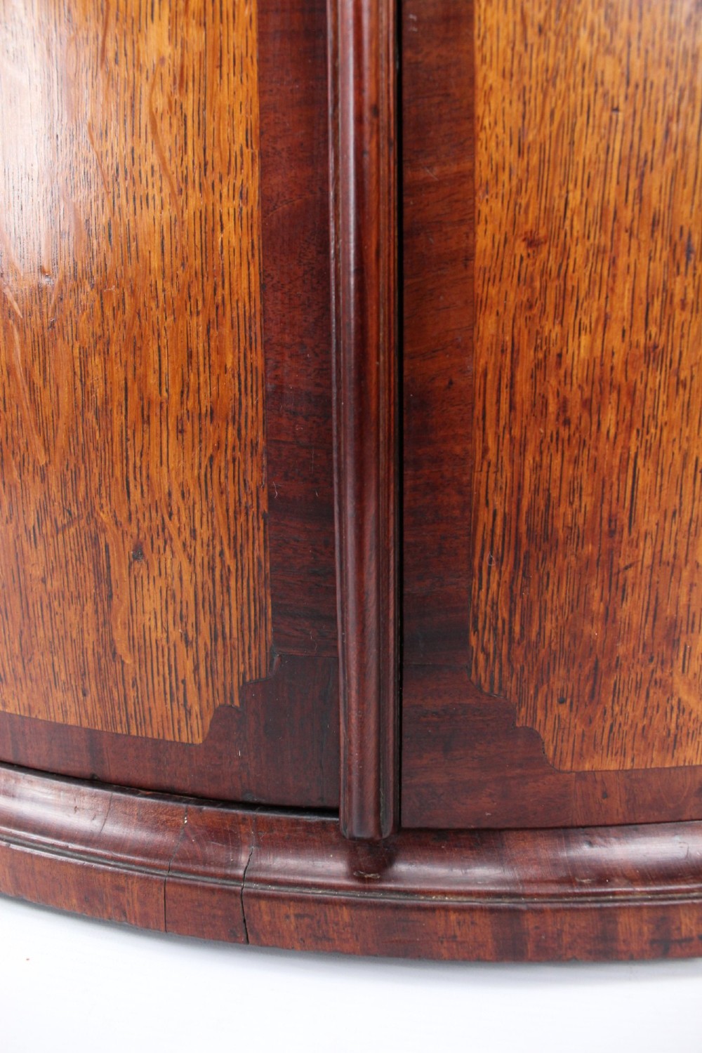 An 18th-century Georgian oak corner cupboard featuring a curved bow front, brass H-hinges, keyhole escutcheon plates, and mahogany crossbanding. View XII