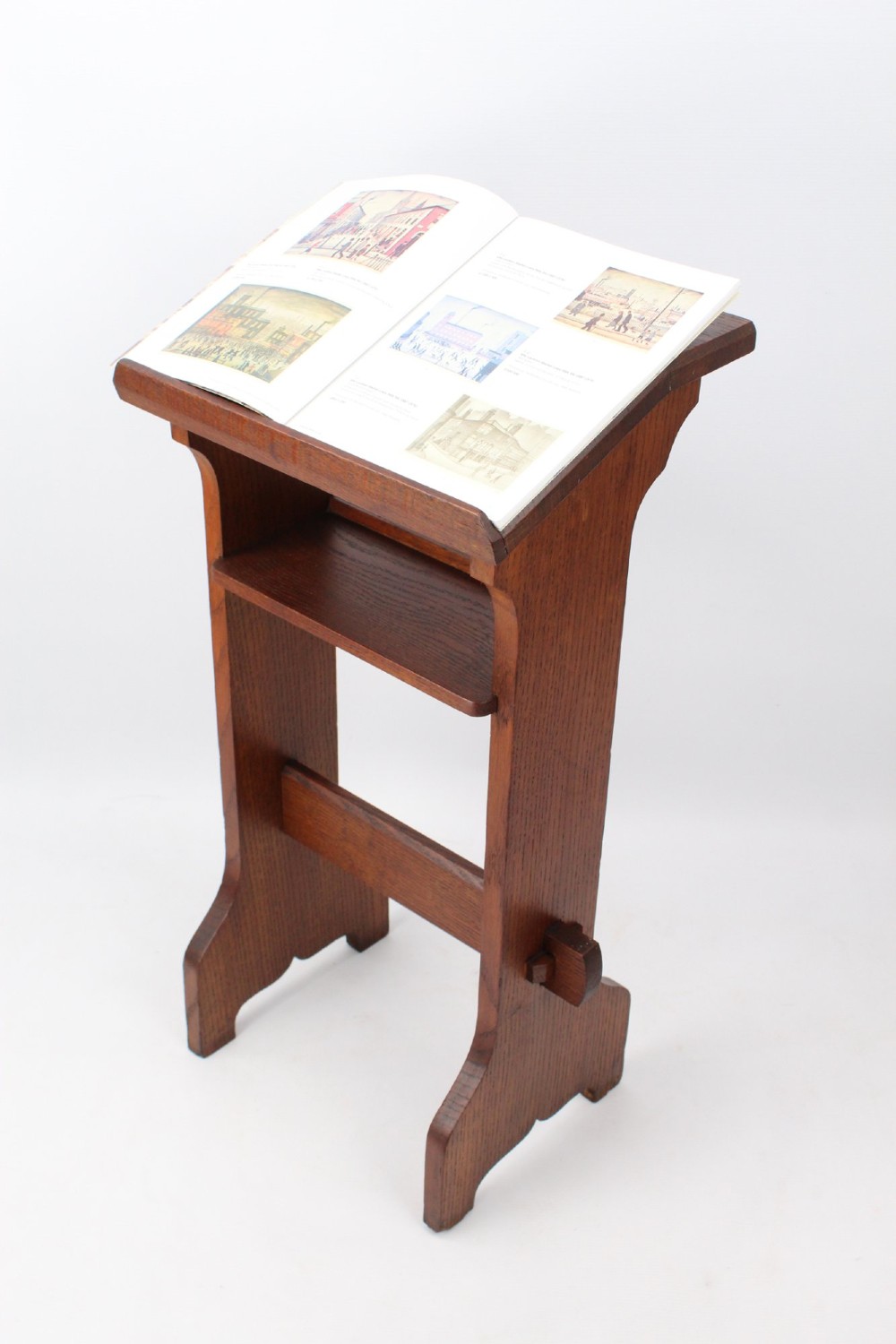 An Edwardian Arts and Crafts solid oak lectern featuring an angled reading top, an open middle shelf, and visible wedge tenon joinery. View II