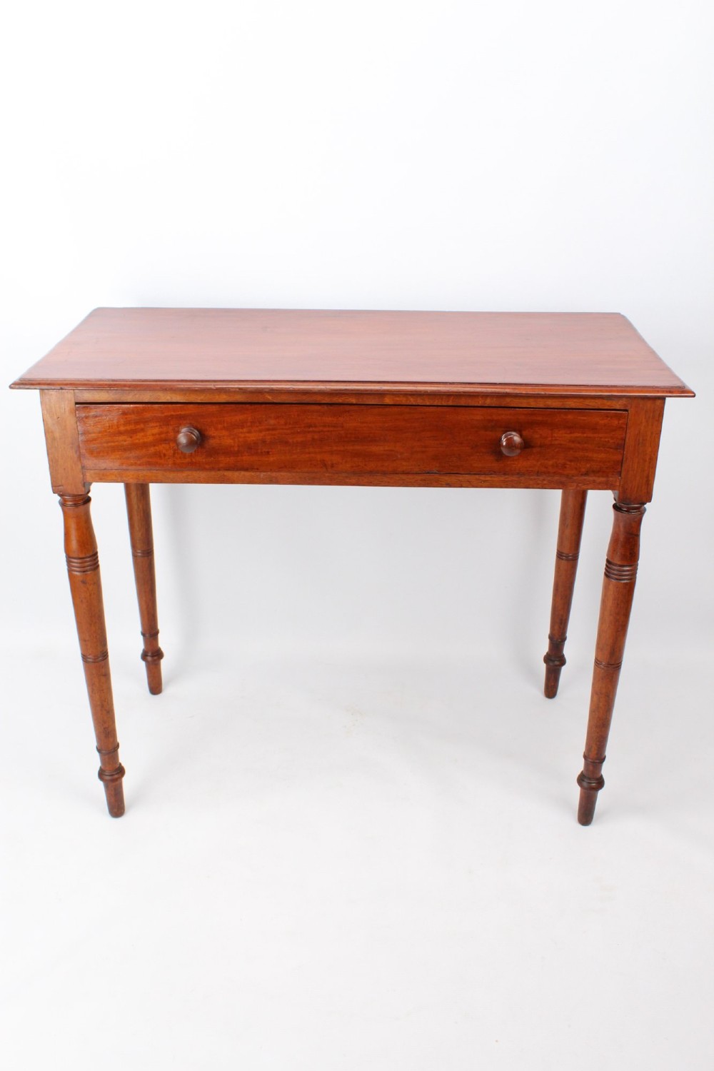 A Victorian mahogany writing table featuring a long frieze drawer with two turned wooden knobs, elevated on four ring-turned tapered legs.