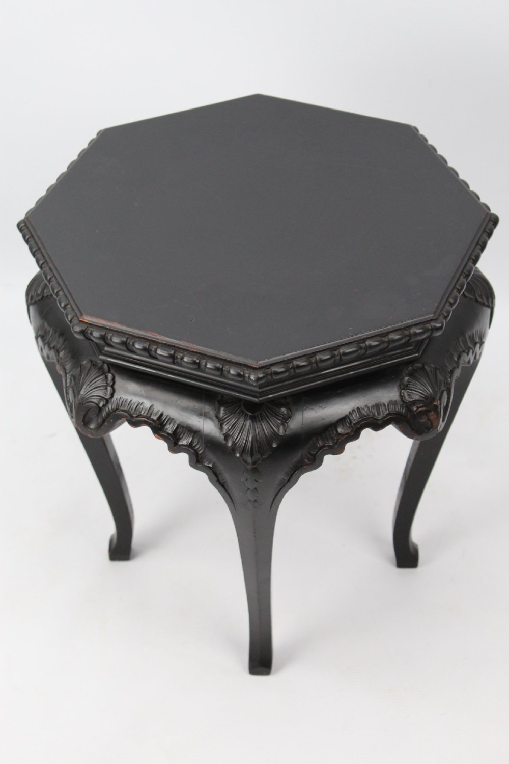 An antique ebonised hexagonal wooden coffee table featuring carved shell details along the apron and cabriole legs against a white background.