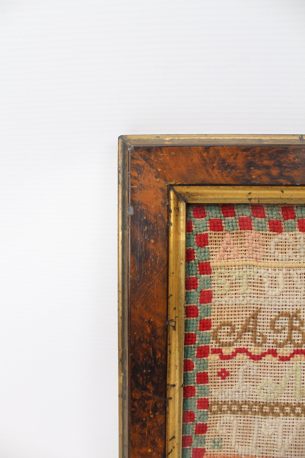 A framed 1875 Victorian needlework sampler featuring rows of embroidered alphabets, geometric borders, and text reading Mary J Garbutt Aged 12 Years inside a wooden frame. View V