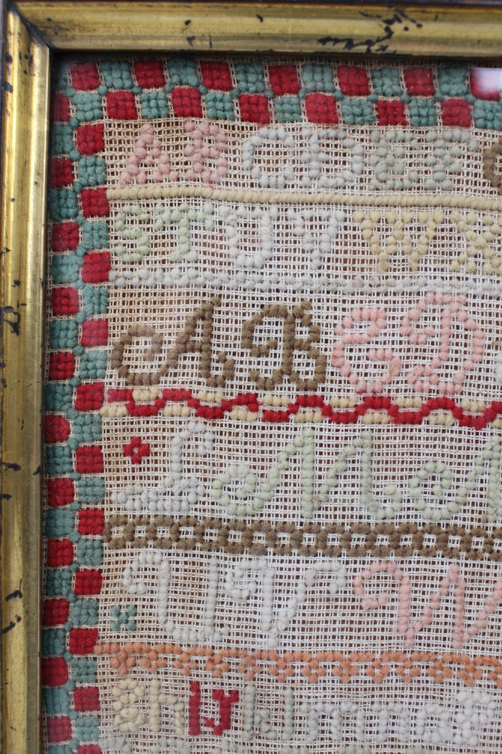 A framed 1875 Victorian needlework sampler featuring rows of embroidered alphabets, geometric borders, and text reading Mary J Garbutt Aged 12 Years inside a wooden frame. View IX