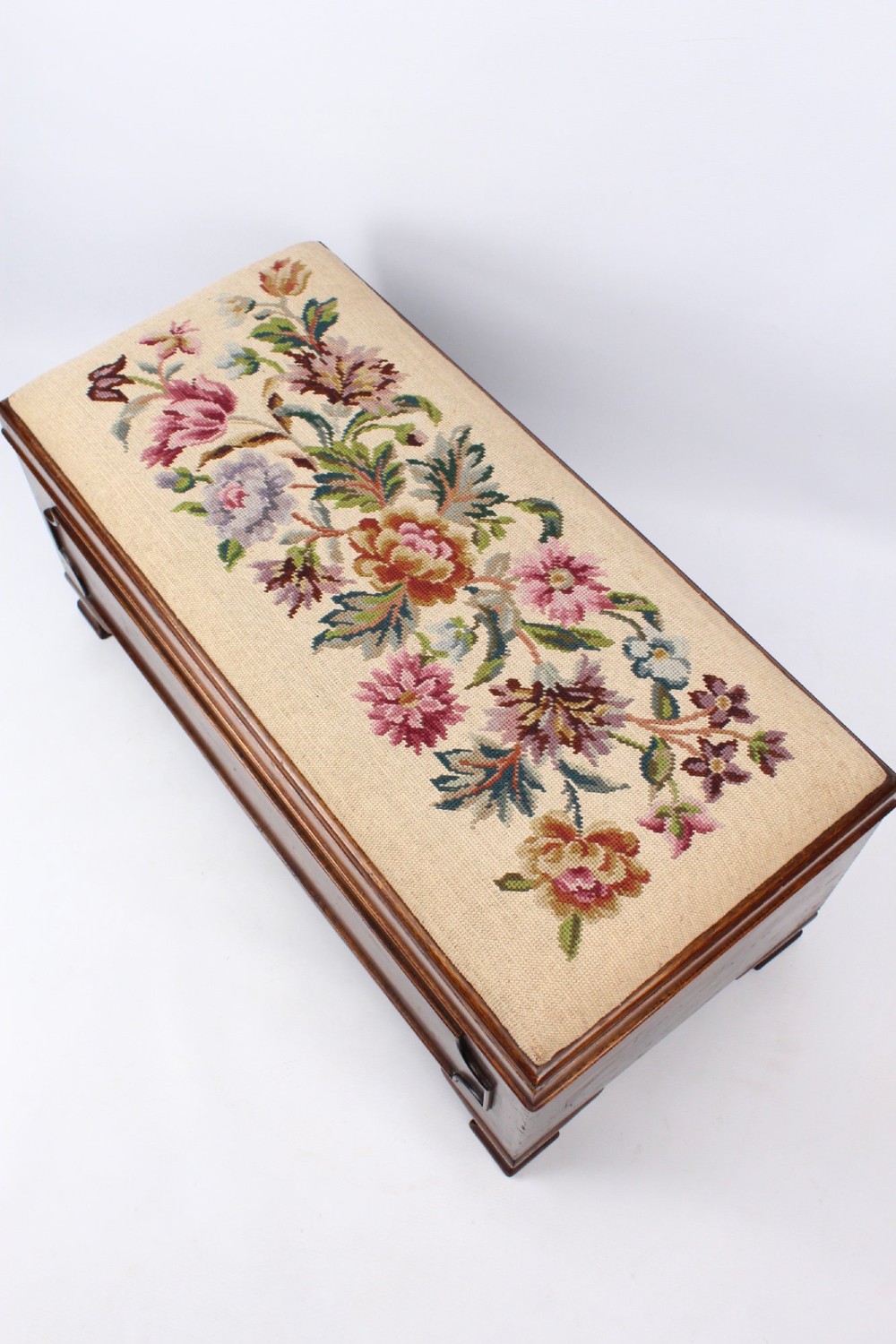 A low rectangular dark mahogany storage ottoman featuring a beige upholstered top with floral needlework embroidery. View V