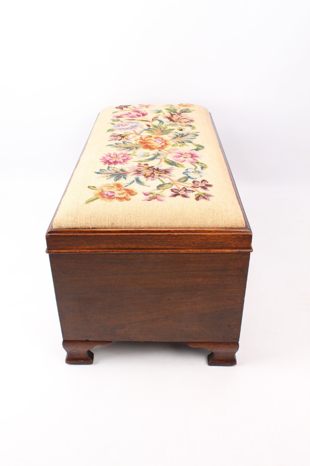 A low rectangular dark mahogany storage ottoman featuring a beige upholstered top with floral needlework embroidery. View VIII