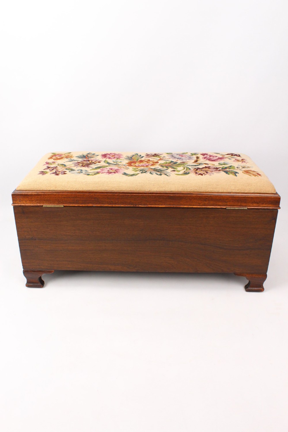 A low rectangular dark mahogany storage ottoman featuring a beige upholstered top with floral needlework embroidery. View IX