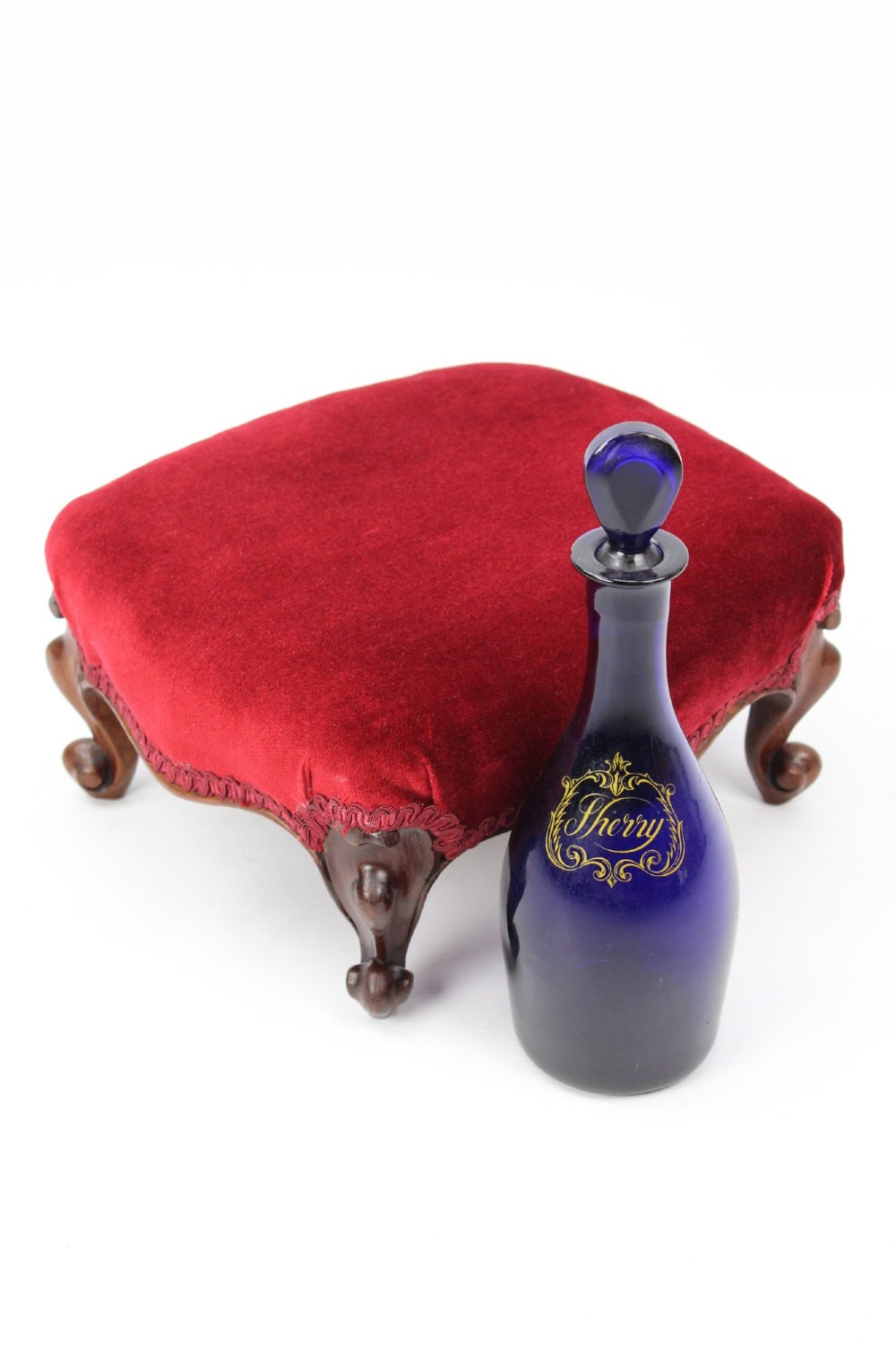 A pair of small Victorian footstools featuring crimson red velvet upholstery and carved walnut cabriole feet. View V