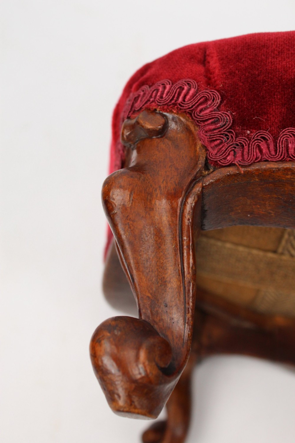 A pair of small Victorian footstools featuring crimson red velvet upholstery and carved walnut cabriole feet. View X