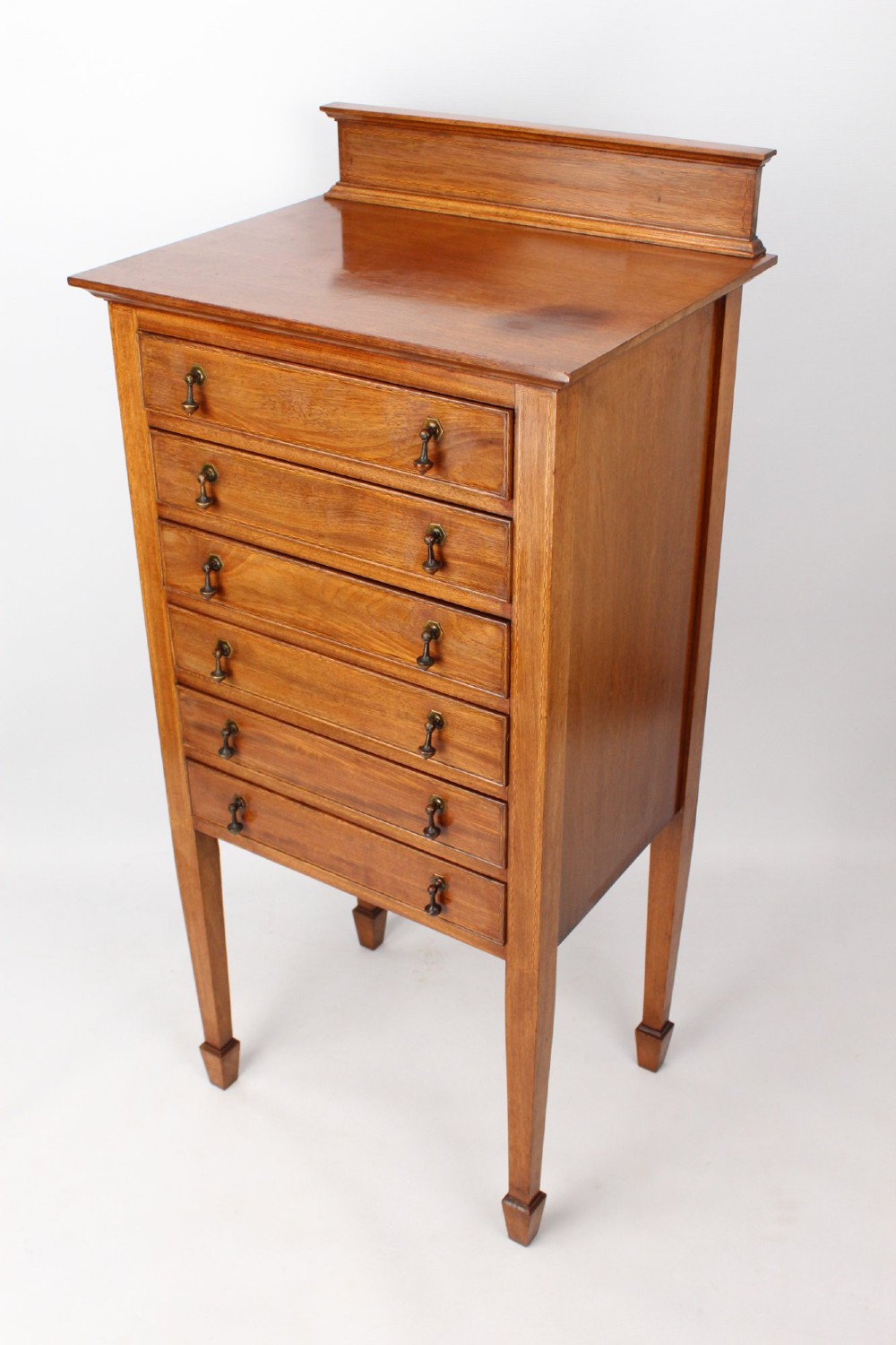 An Edwardian mahogany music cabinet featuring six shallow drawers with brass handles, set on slender square tapered legs with a raised gallery back. View II
