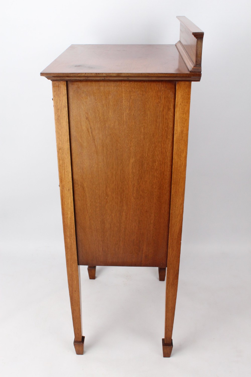 An Edwardian mahogany music cabinet featuring six shallow drawers with brass handles, set on slender square tapered legs with a raised gallery back. View III