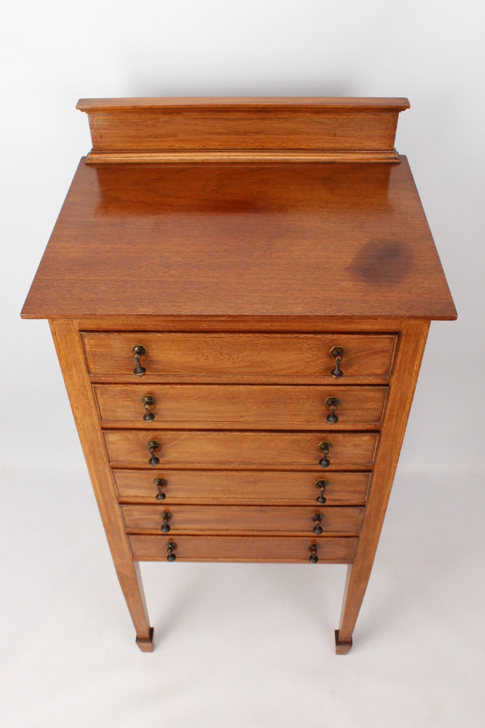 An Edwardian mahogany music cabinet featuring six shallow drawers with brass handles, set on slender square tapered legs with a raised gallery back. View IV