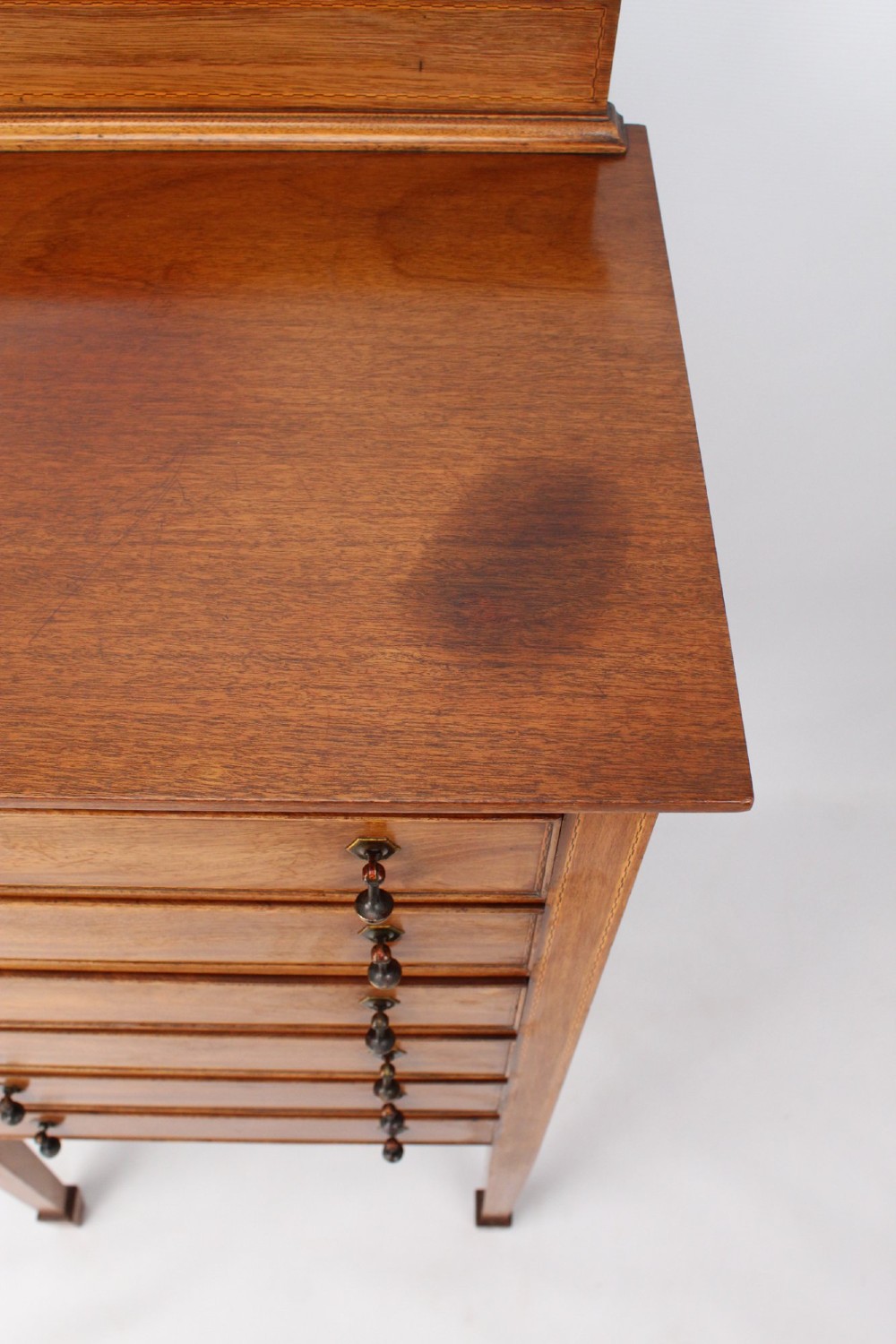 An Edwardian mahogany music cabinet featuring six shallow drawers with brass handles, set on slender square tapered legs with a raised gallery back. View V
