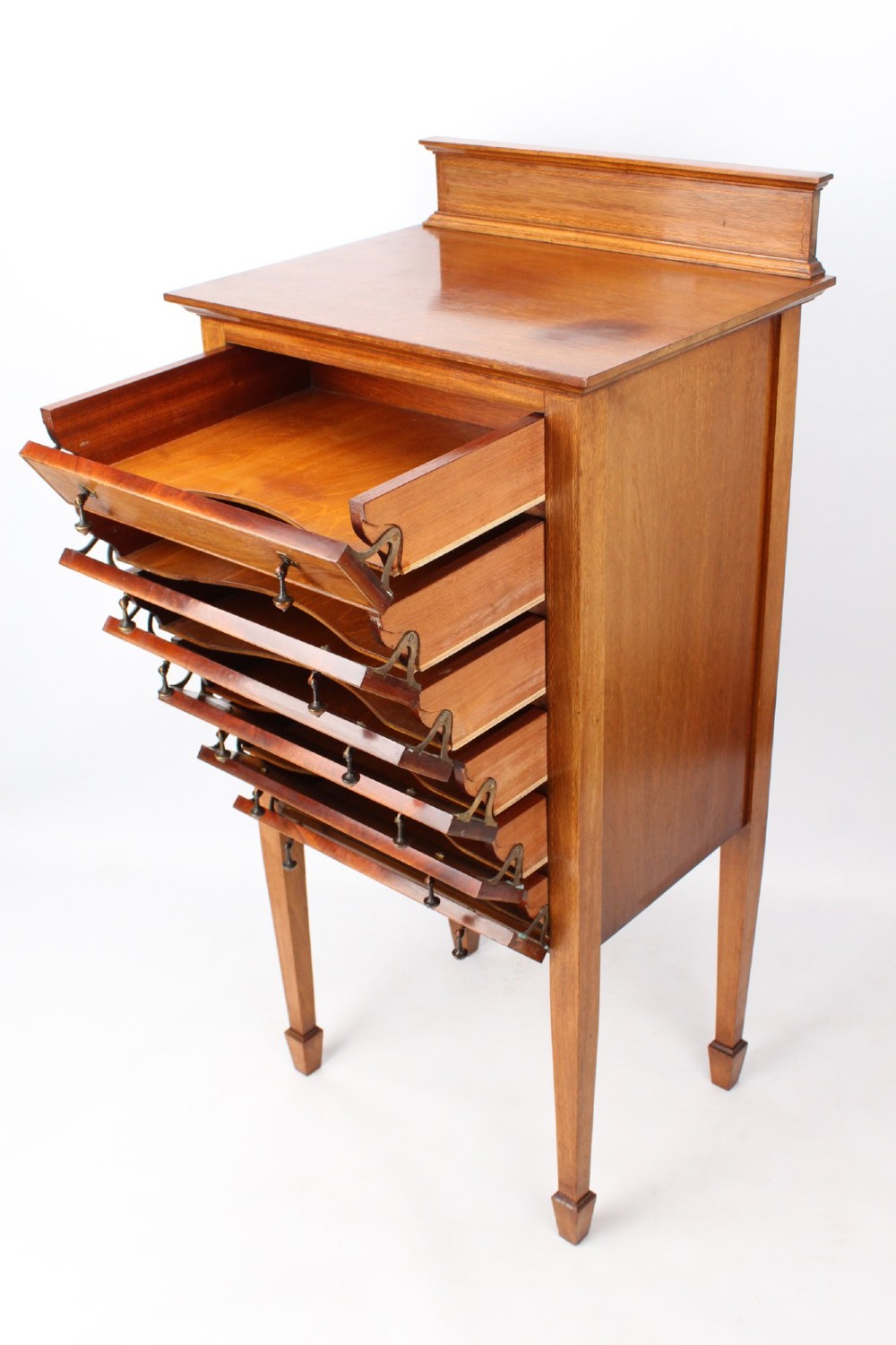 An Edwardian mahogany music cabinet featuring six shallow drawers with brass handles, set on slender square tapered legs with a raised gallery back. View VI