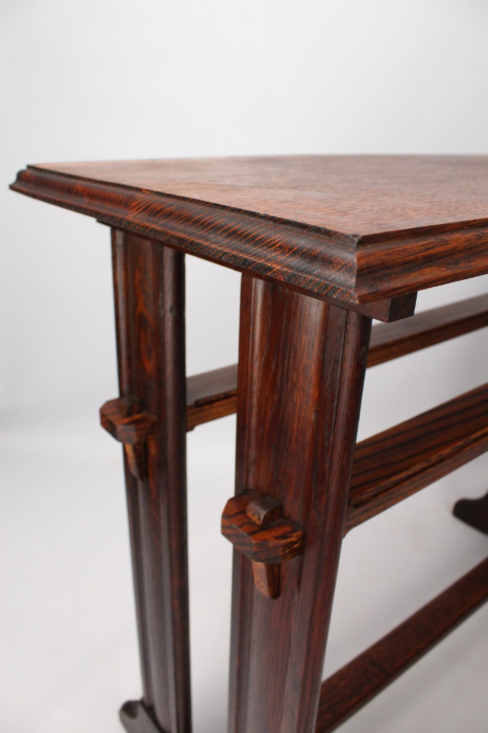 An Edwardian Arts and Crafts medium brown oak side table featuring double upright supports, exposed joint details, and a low stretcher. View X