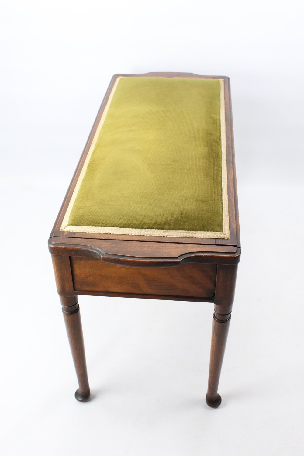 An Edwardian wooden duet piano stool featuring an olive green velvet upholstered seat and slender tapered legs. View V