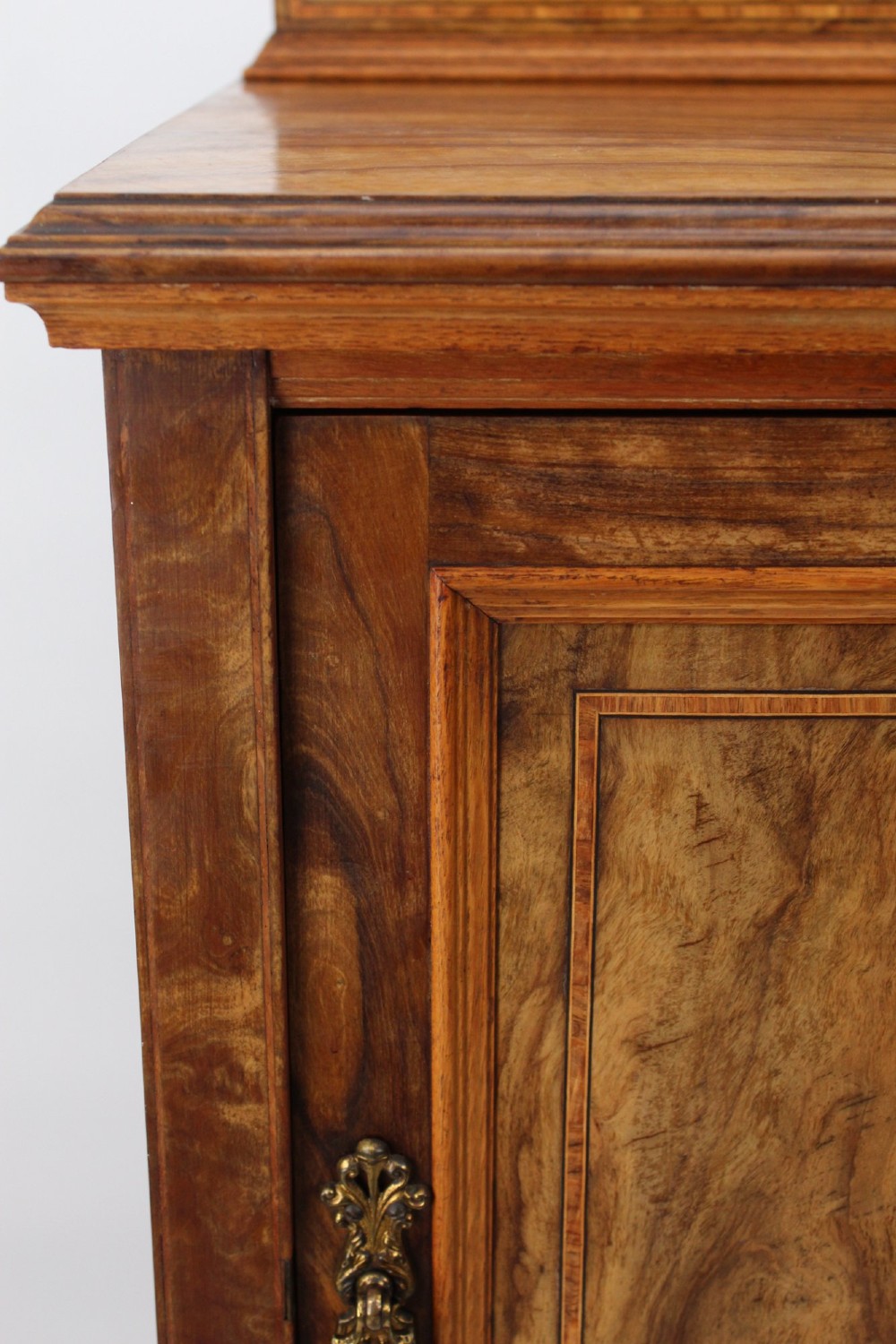 An Edwardian burr walnut bedside cabinet featuring a small gallery top, crossbanded inlaid door panel, drop brass handle, and square tapered legs. View X